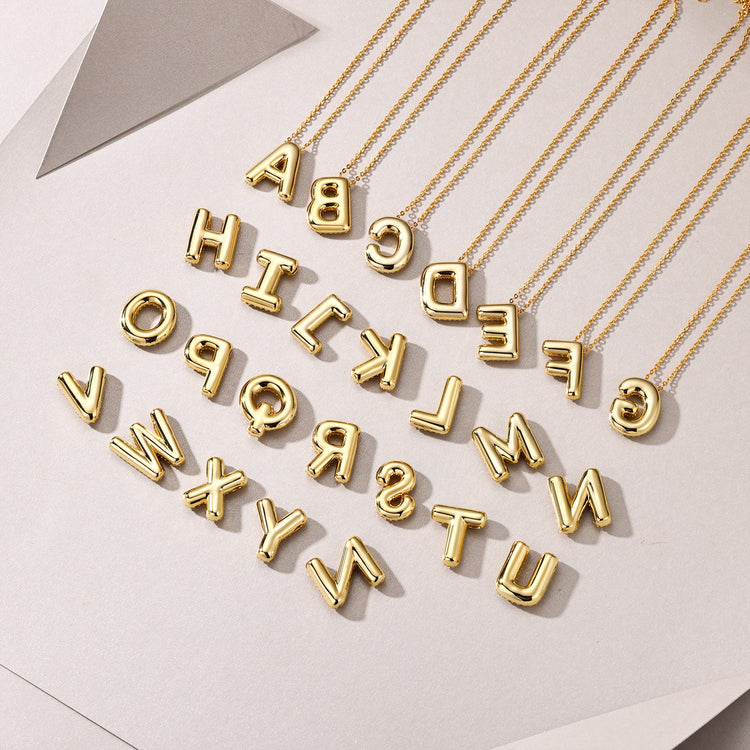 Personalized moissanite initial necklace featuring gold-plated bubble letters on a geometric background.