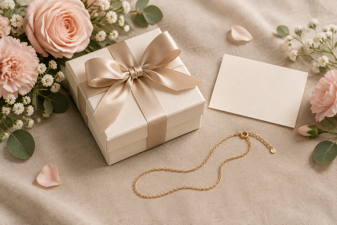 Illustrative birthday jewelry gift box with champagne ribbon, a blank card, and blush flowers on linen.