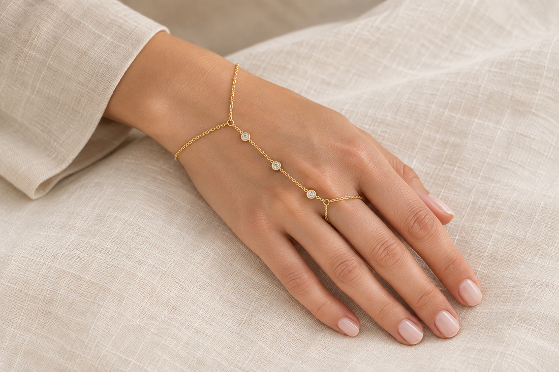 Delicate gold-tone hand chain connecting a wrist bracelet to a finger loop on a hand resting on ivory linen.