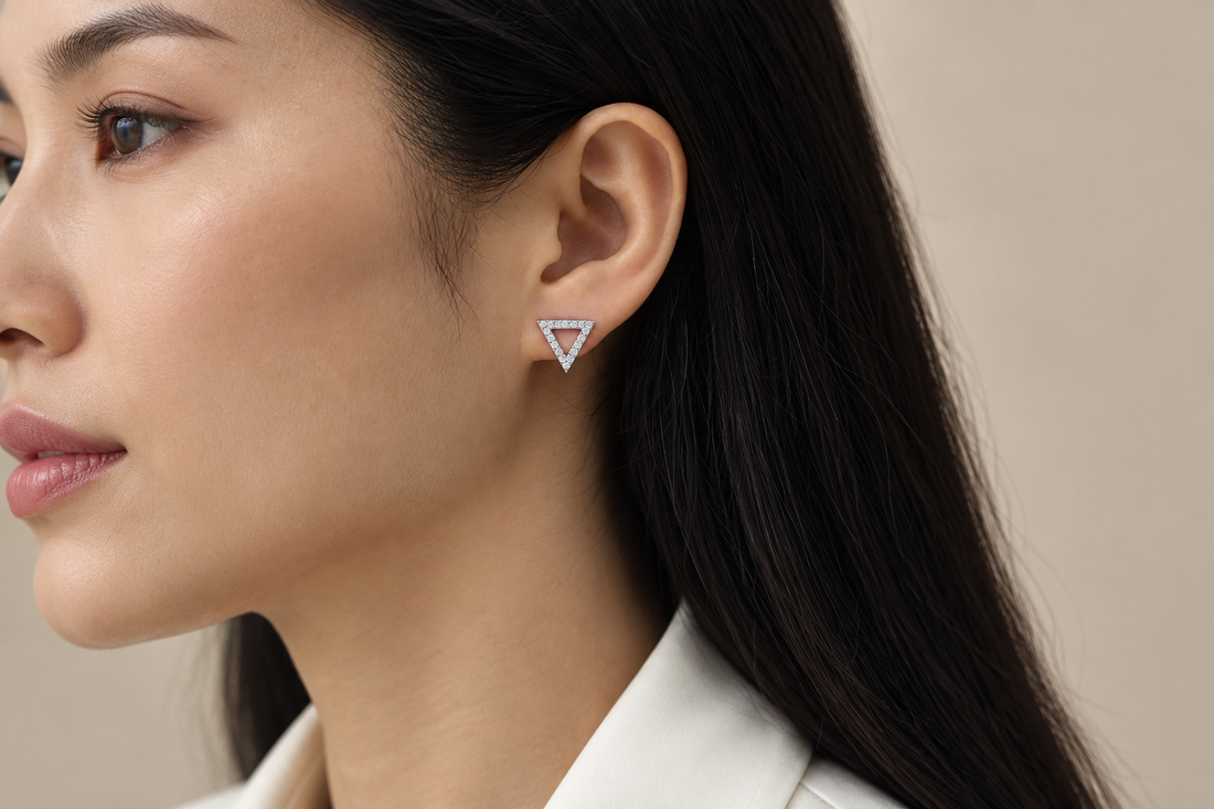 Silver-tone open triangular moissanite stud earring styled with tucked-back hair and an ivory shirt.