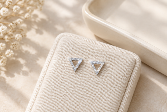 Pair of silver-tone open triangular gemstone stud earrings arranged on ivory linen beside a cream tray.