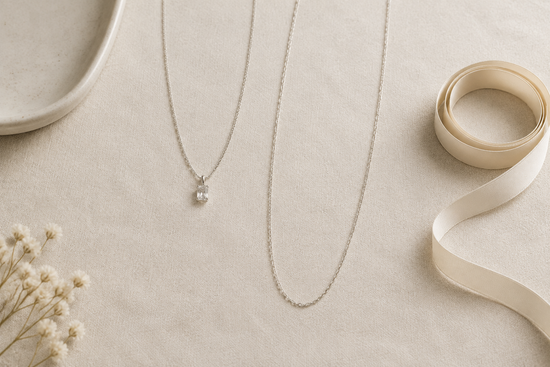 Illustrative necklaces arranged at different lengths on ivory linen beside a plain measuring ribbon.