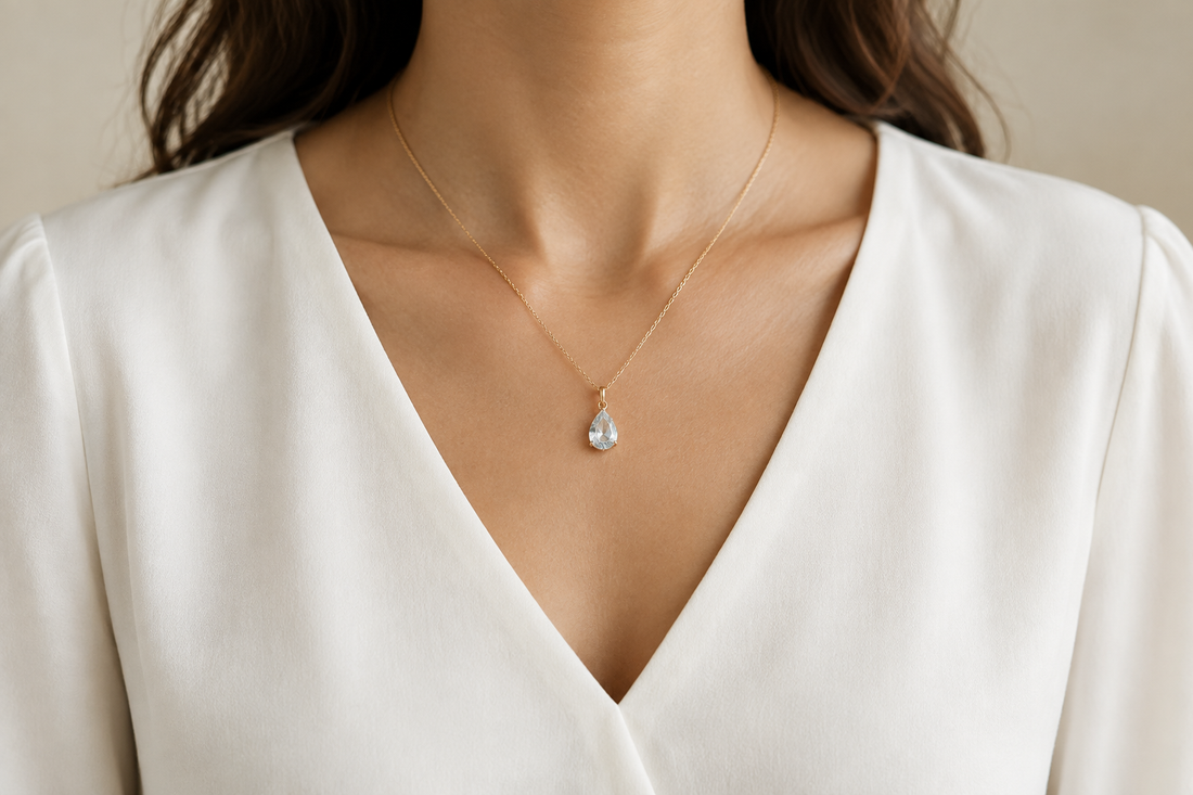 Illustrative gold-tone drop pendant worn above the neckline of an ivory V-neck blouse.
