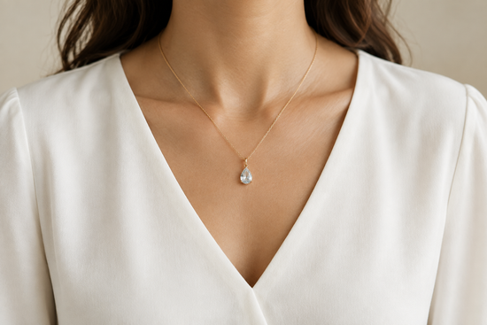 Illustrative gold-tone drop pendant worn above the neckline of an ivory V-neck blouse.