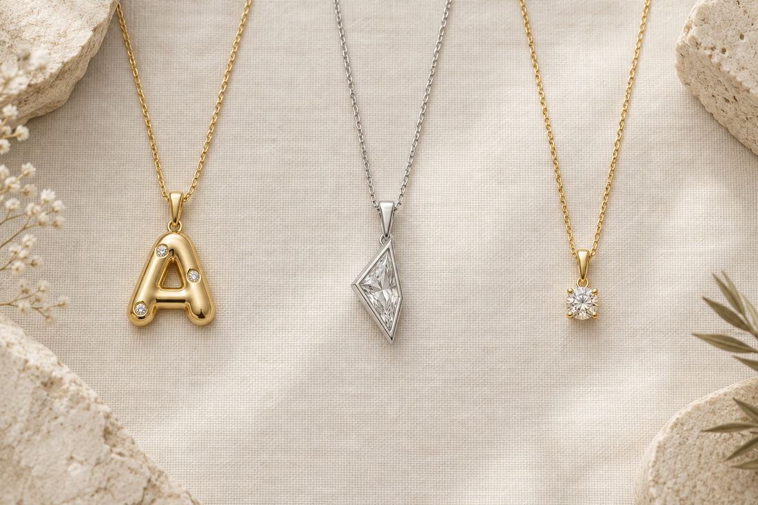 Illustrative initial, geometric, and solitaire-style gemstone necklaces arranged separately on ivory linen.