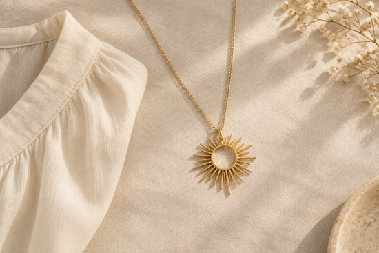 Illustrative gold-tone open sunburst pendant necklace arranged on ivory linen beside a cream blouse.