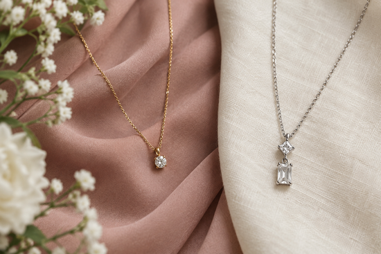 Illustrative gold-tone and silver-tone gemstone necklaces on dusty rose fabric and ivory linen beside flowers.